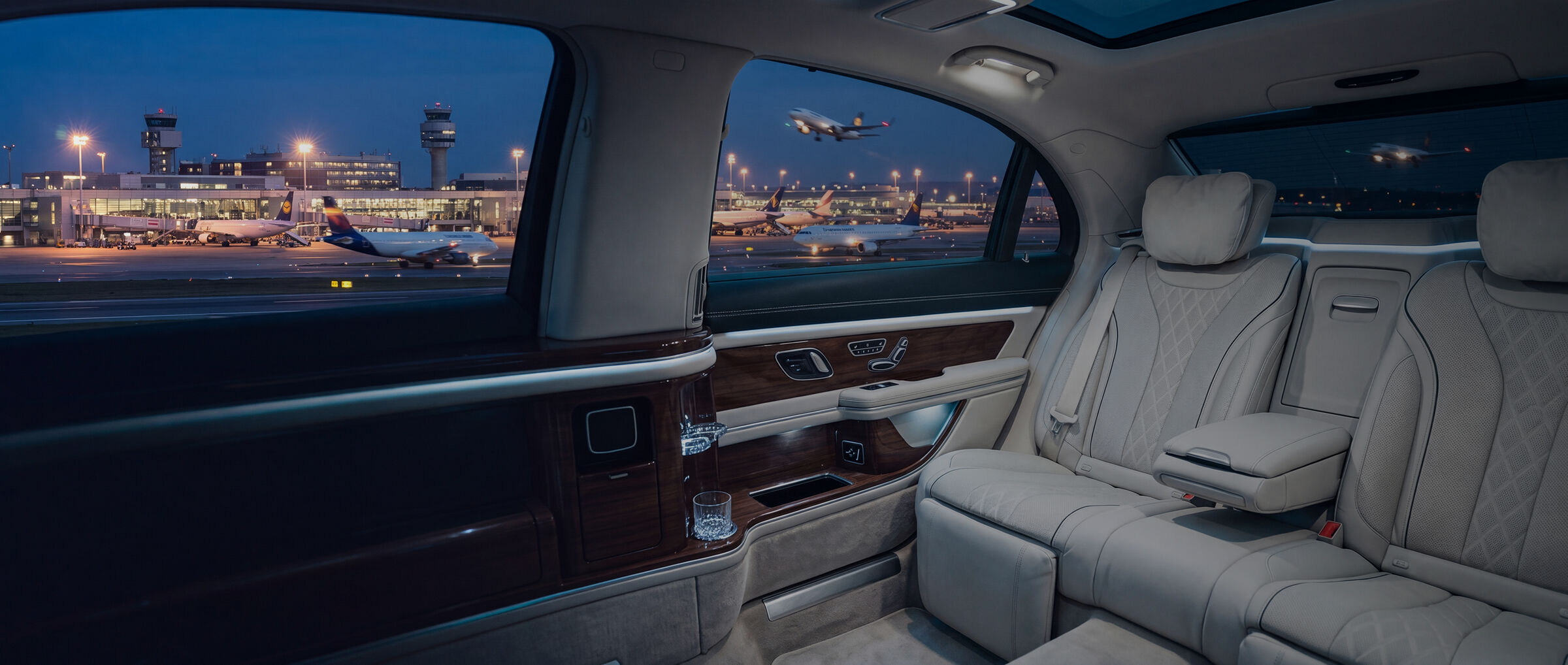 Fond einer Limousine mit hellen Ledersitzen, draussen ein Flughafen bei Nacht