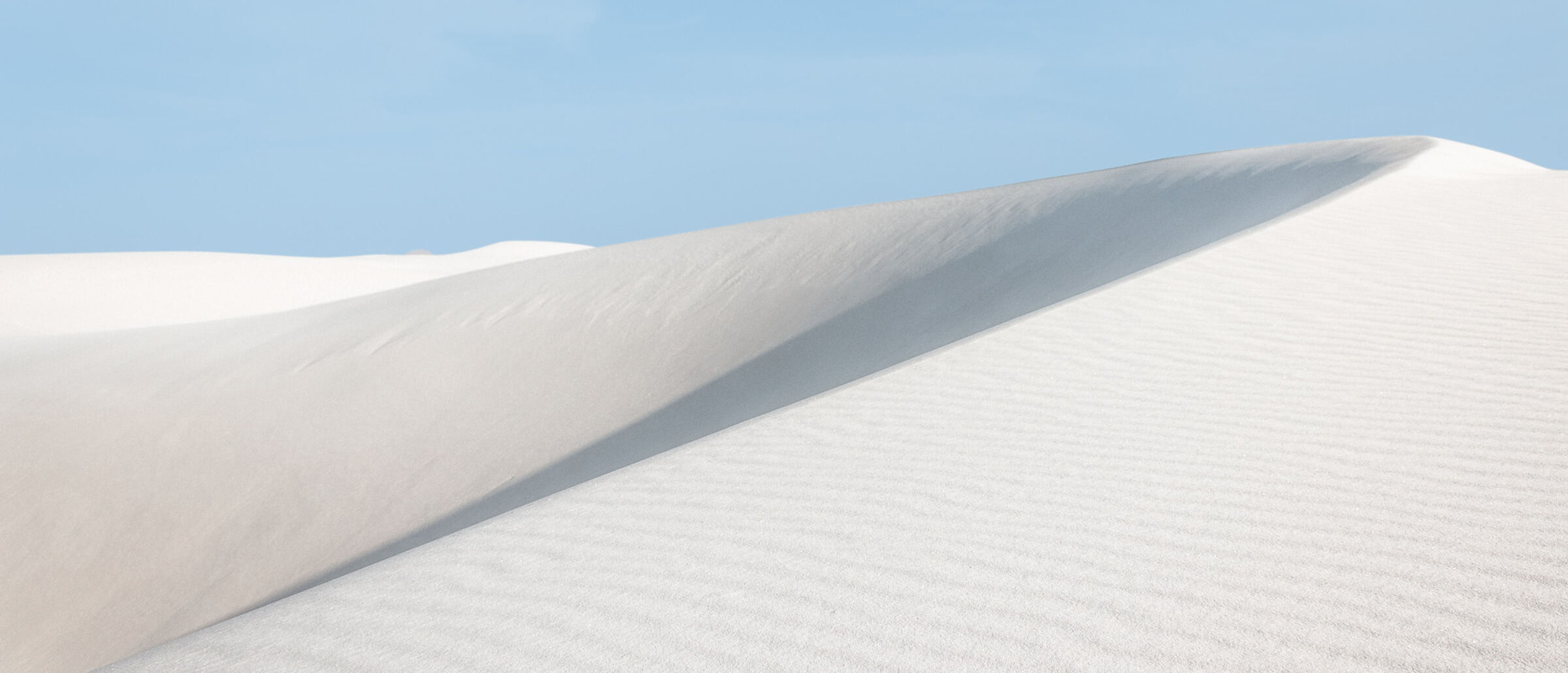 Feine weisse Sanddüne unter klarem Himmel, Sinnbild für reine, frische Luft