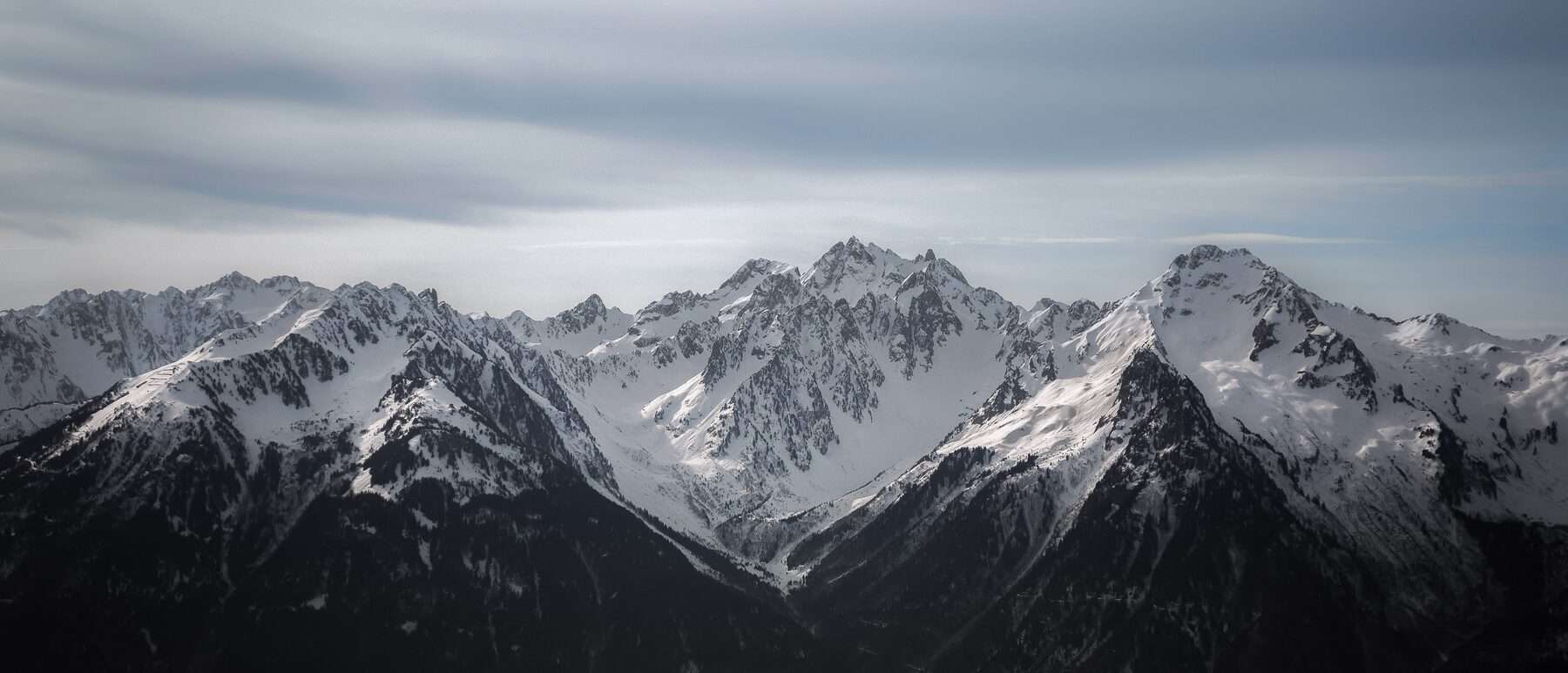 Verschneite Alpenkette unter bedecktem Himmel